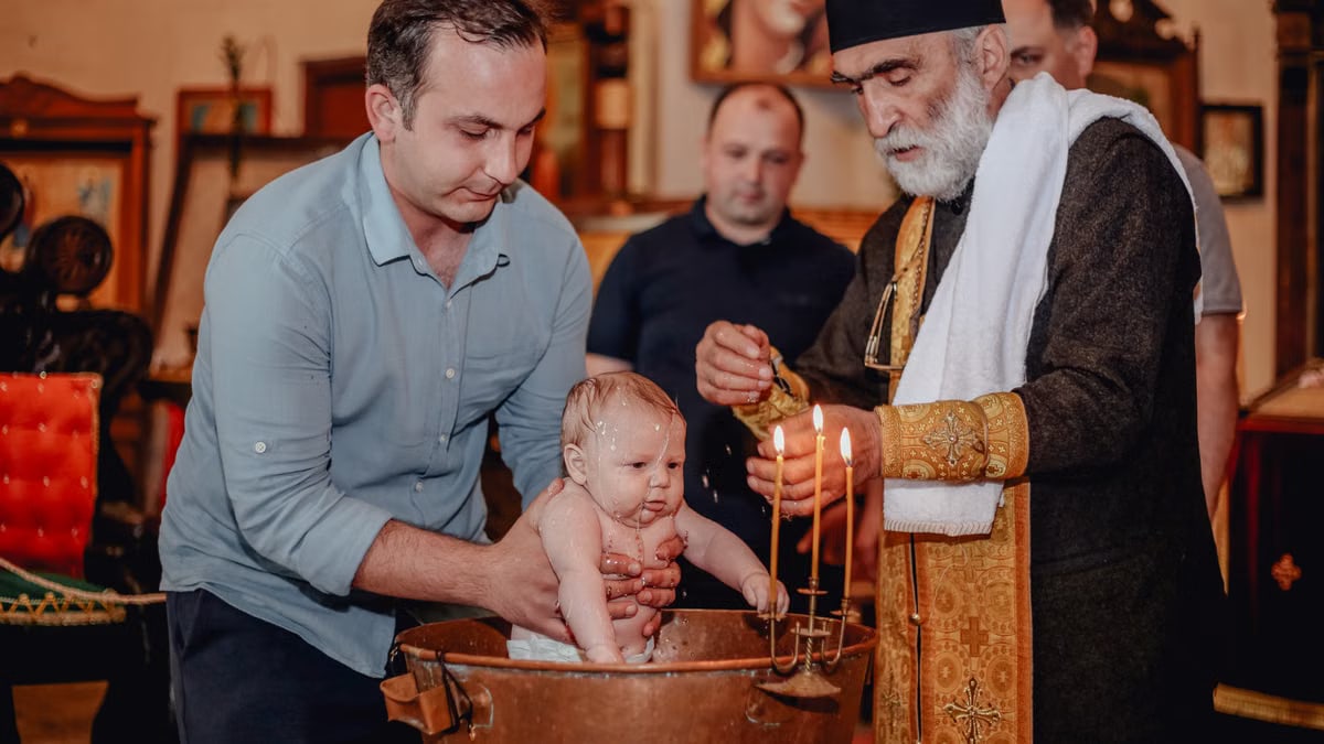 Baptism ceremony with a priest lighting candles, surrounded by family, indoors.